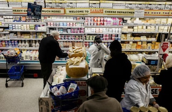 Una vista interior del departamento de quesos de Zabar's, donde clientes y empleados se mueven entre estantes repletos de productos lácteos y grandes quesos