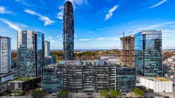 Vista aérea de edificios acristalados de gran altura, una construcción con grúa, calles con árboles y vegetación costera bajo el cielo azul