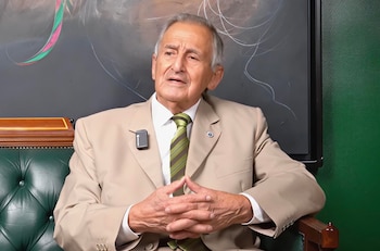 Retrato de General Juan Antonio Herrera Betancourt, hombre mayor de cabello gris, traje beige, corbata, sentado en sillón verde de cuero con micrófono
