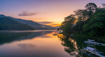 Un lago rodeado de montañas y árboles bajo un cielo de tonos naranjas y morados. Varios botes filipinos de madera con estabilizadores flotan en el agua.