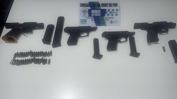 Cuatro pistolas negras, varios cargadores y balas sobre una superficie blanca. Al fondo, un cartel de la Comisaría Sur 3ra. Virrey del Pino con "ARMAS DE FUEGO"