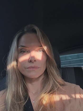 Primer plano de una mujer de cabello largo rubio sentada en el asiento de un automóvil. Un haz de luz solar diagonal cruza su rostro