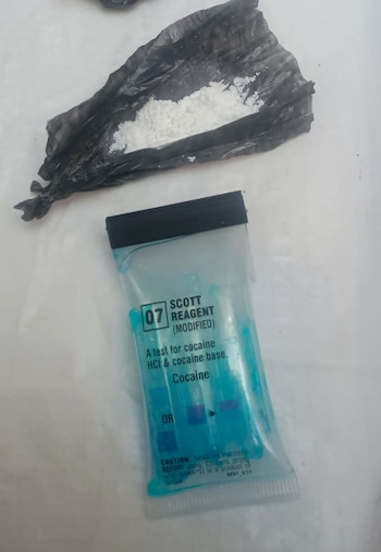 Primer plano de una sustancia blanca en polvo dentro de una bolsa de plástico negra, junto a un kit de prueba de cocaína "Scott Reagent"