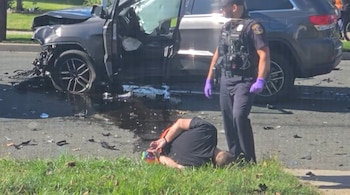 Un policía con chaleco táctico permanece junto a un hombre esposado en el suelo y una camioneta gris chocada