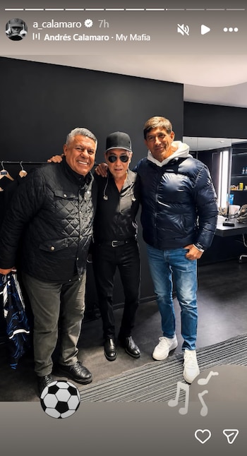 Andrés Calamaro, con gorra negra y gafas, Chiqui Tapia, con chaqueta acolchada oscura, y un tercer hombre, sonríen mientras posan en un backstage oscuro