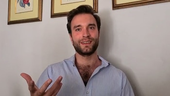 Retrato de un hombre caucásico joven con barba, camisa de rayas azules y blancas, gesticulando. Detrás, una pared blanca con dos cuadros enmarcados