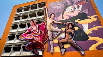 Tres bailarinas con vestimentas folclórica, de ballet y urbana posan ante la fachada de un edificio naranja con un mural ilustrado.