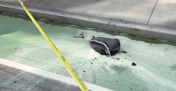 Una mochila negra y una prenda clara yacen sobre una ciclovía verde delimitada por una cinta amarilla de precaución