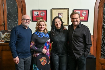 Cuatro personas sonríen juntas en un recinto con reconocimientos musicales y cuadros colgados en la pared