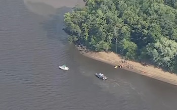 Vista aérea de un río con dos embarcaciones pequeñas junto a una orilla de vegetación densa donde hay varias personas