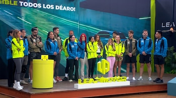 Un grupo de diecisiete personas de pie en un escenario con uniformes de colores azul, negro y amarillo neón, junto a un logo de Leap Motor y un podio amarillo.