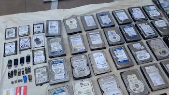 Decenas de discos duros de computadora, memorias USB y tarjetas de memoria dispuestas en filas sobre una tela blanca