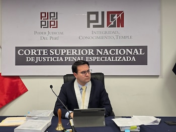 El juez Eiser Alexander Jiménez Coronel sentado ante un escritorio con expedientes, un micrófono y la insignia del Poder Judicial del Perú