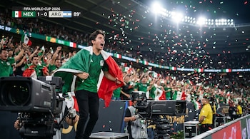 Un joven hincha mexicano celebra con su bandera en un estadio iluminado, rodeado de confeti y otros aficionados, con cámaras de televisión en primer plano.