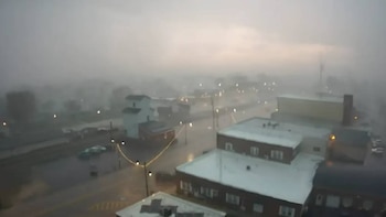 Vista aérea de un paisaje urbano cubierto por una densa niebla o calima, con techos de edificios, calles y algunas luces tenuemente visibles a través de la neblina