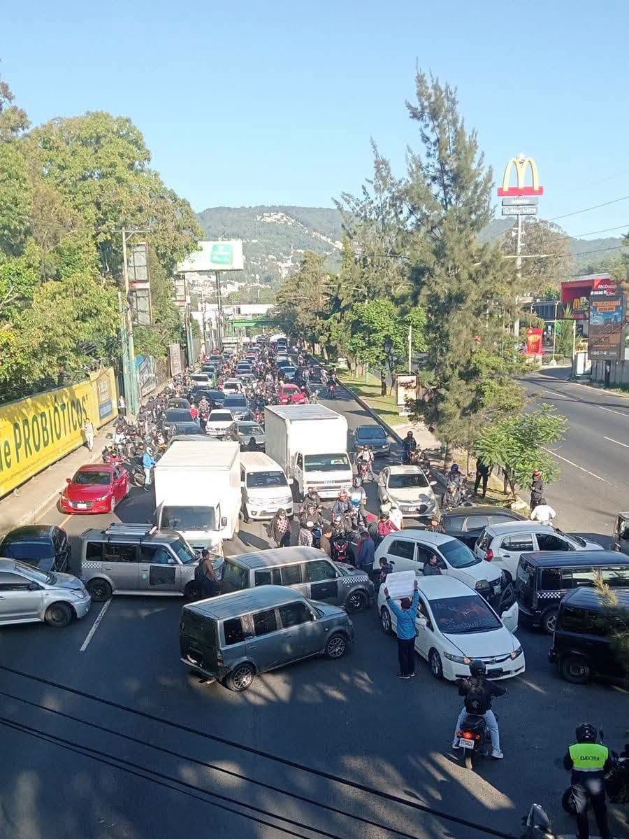 Una manifestación en la calle genera un embotellamiento vehicular con automóviles, camionetas y motocicletas detenidos en una vía urbana. (Sololá Informativo Digital)