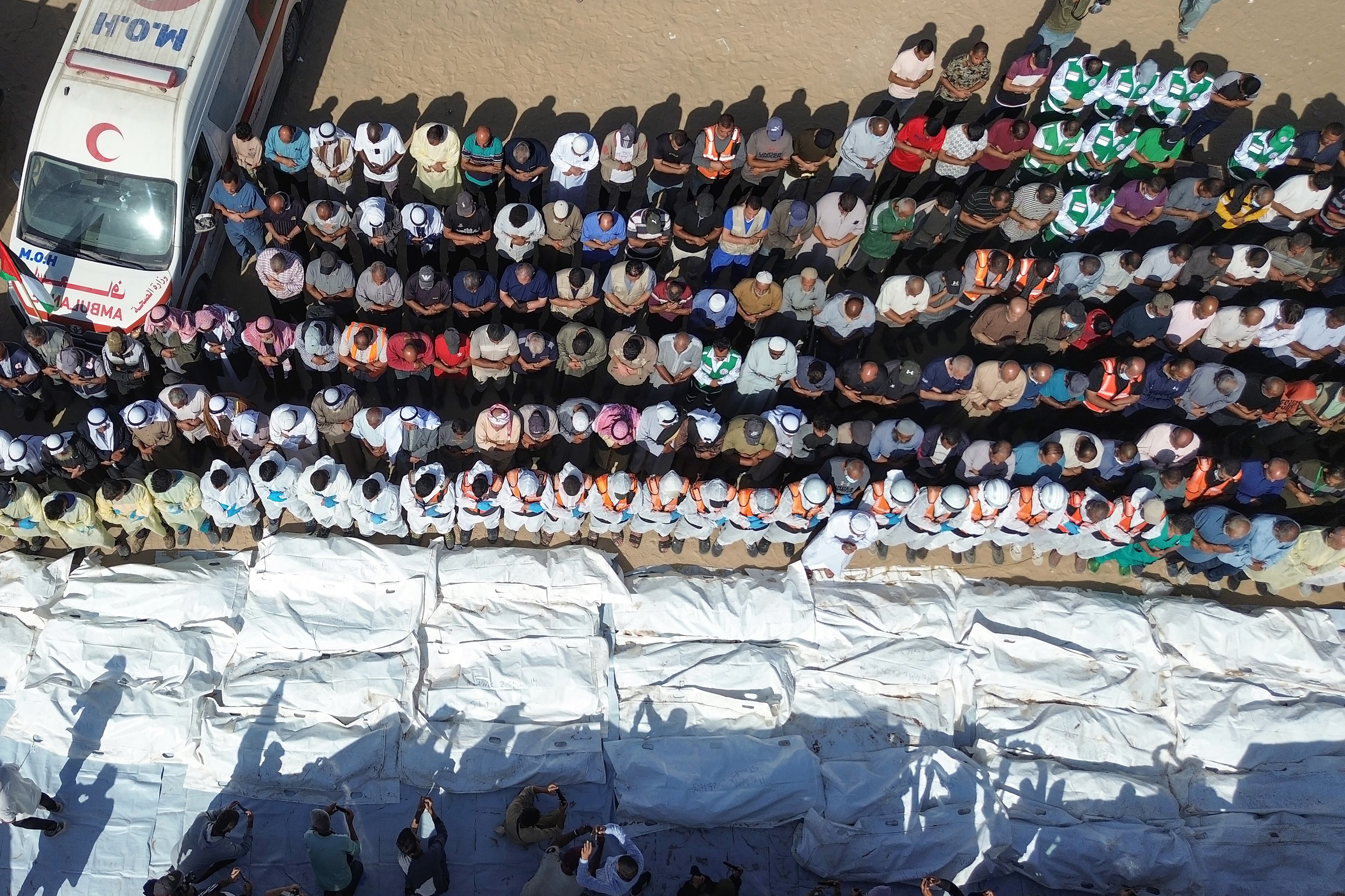 Equipos médicos rezan junto a los restos y cuerpos de palestinos no identificados, devueltos por Israel, antes de su entierro masivo fuera del Hospital Nasser en Khan Yunis, Franja de Gaza sur, 22 de octubre de 2025. (EFE/EPA/HAITHAM IMAD)