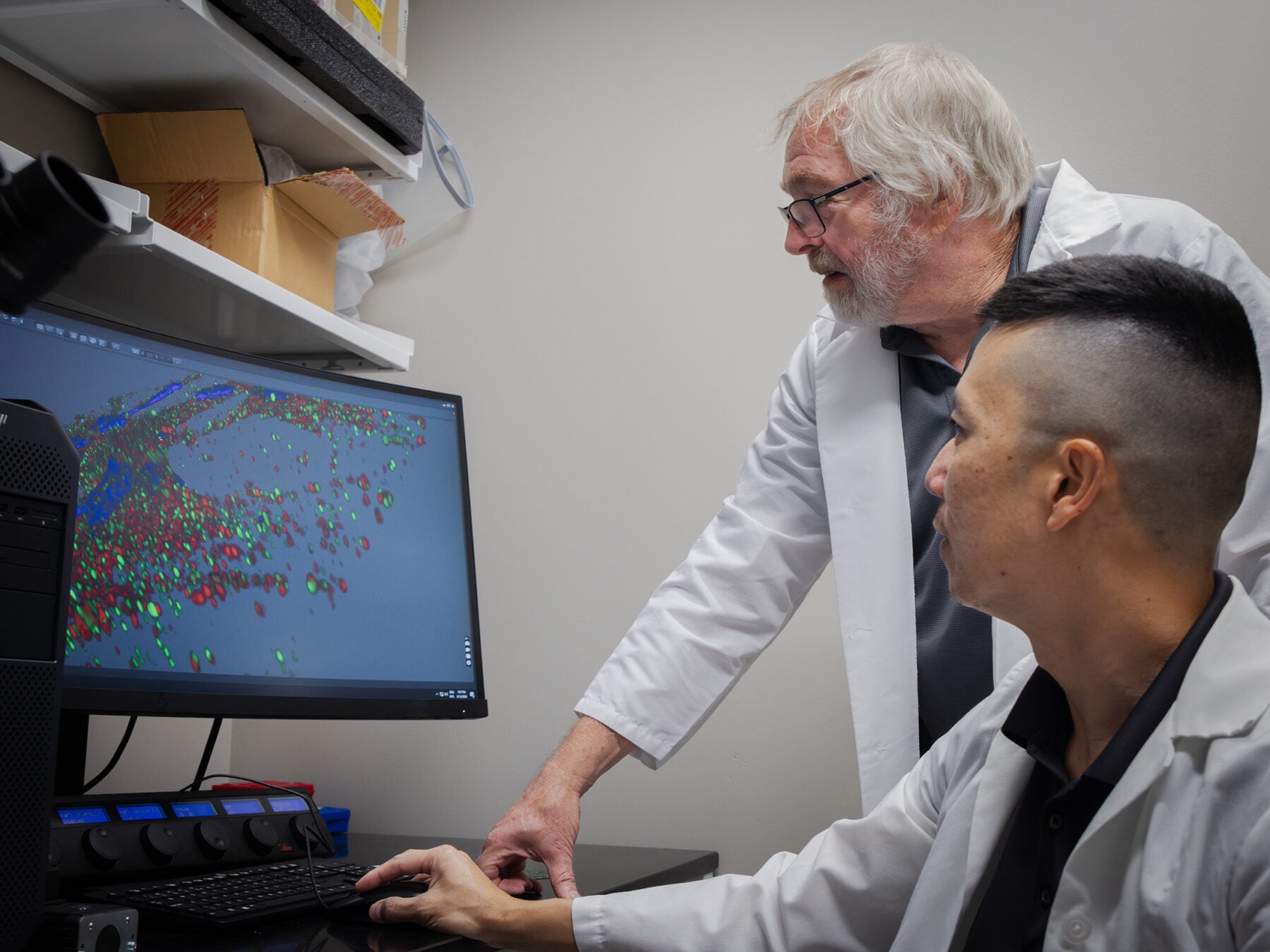 Dos investigadores con batas de laboratorio observan una proyección celular tridimensional en la pantalla de una computadora. (Universidad de Texas A&M)