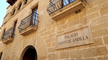 Fachada de piedra con balcones de hierro forjado, arcos en la parte superior y una placa de piedra inscrita con Palacio Barón de Andilla.