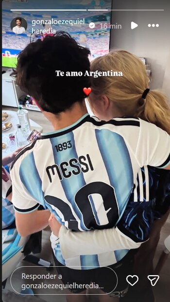 Un hombre de espaldas con camiseta de fútbol argentina número 10 de Messi abraza a una mujer de cabello rubio, con mesas y un televisor de fondo