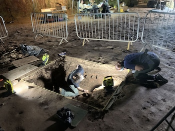 Dos arqueólogas excavan un foso iluminado dentro del Castillo de Pembroke, rodeadas de equipos, barreras metálicas y personal en el fondo