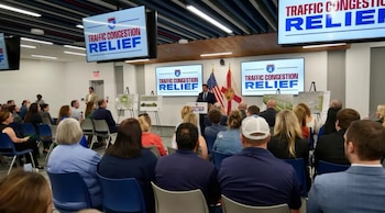 El gobernador DeSantis habla en un podio ante una audiencia. Se ven pantallas con 'TRAFFIC CONGESTION RELIEF' y banderas de EE. UU. y Florida al fondo