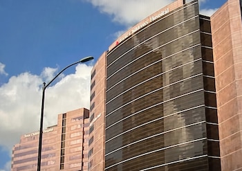 Vista exterior de un edificio alto del Texas Children's Hospital con fachada de vidrio y ladrillo, un poste de luz y cielo azul con nubes
