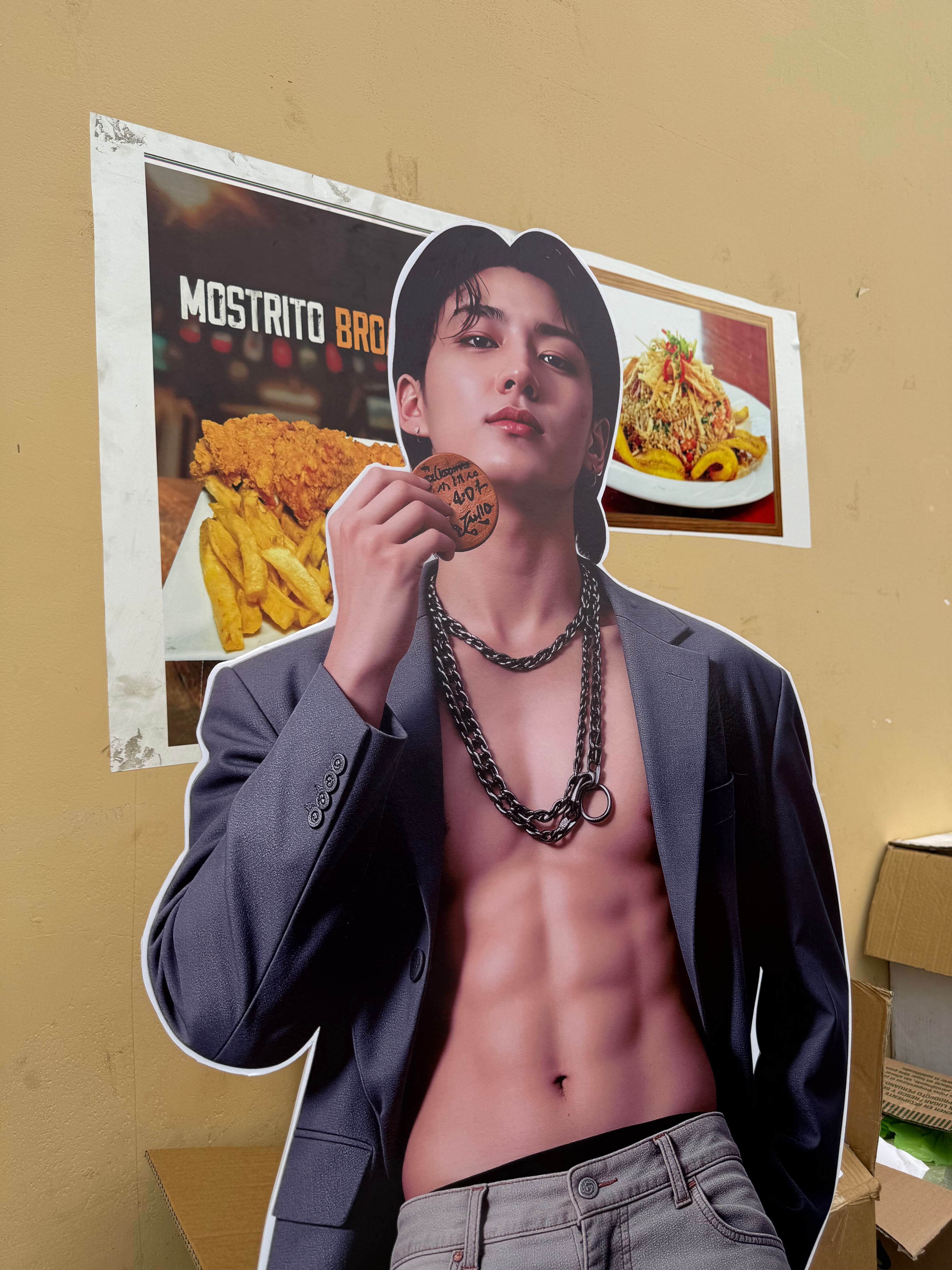 Un recorte publicitario de un integrante de BTS se exhibe junto a afiches gastronómicos en las inmediaciones del Estadio San Marcos durante la venta de productos informales en Lima. (Paula Díaz)