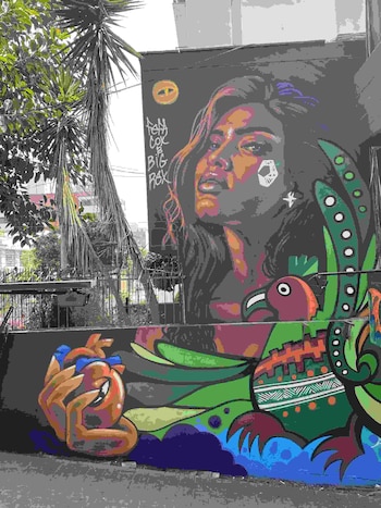 Mural exterior con el rostro de una mujer, un corazón anatómico y un ave estilizada pintados sobre dos muros junto a una palmera