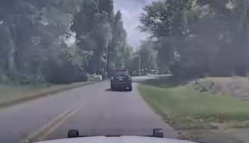 Vista desde un vehículo en movimiento de una SUV oscura circulando por una carretera arbolada bajo un cielo nublado, con vegetación a los lados
