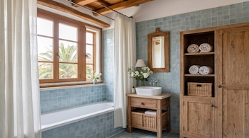 Un cuarto de baño con azulejos azules, bañera blanca, lavabo sobre mueble de madera, espejo, armario y ventanal.