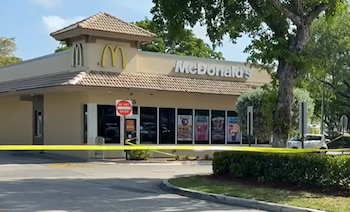 Edificio de McDonald's acordonado con cinta policial amarilla. Se observa un cartel de 'DO NOT ENTER' en la puerta y árboles alrededor