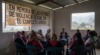 Un grupo de mujeres sentadas en un círculo en una habitación modesta con un cartel que dice "EN MEMORIA DE LAS VÍCTIMAS DE VIOLENCIA SEXUAL EN EL CONFLICTO ARMADO".