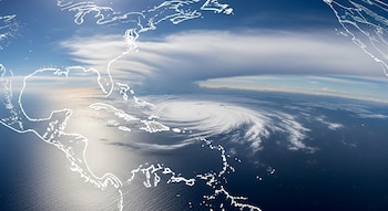 Vista aérea del océano Atlántico con un gran sistema de nubes giratorias, un mapa esquemático de las costas del Caribe y el este de Estados Unidos, y cielo azul con nubes dispersas.