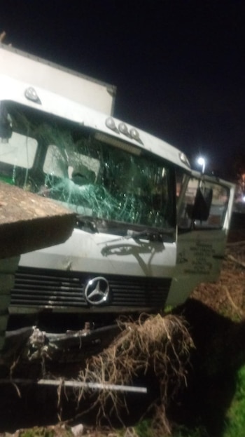 Camión comercial Mercedes-Benz blanco con parabrisas destrozado, logotipo en la parrilla, escombros en el frente y el suelo, visible en la oscuridad