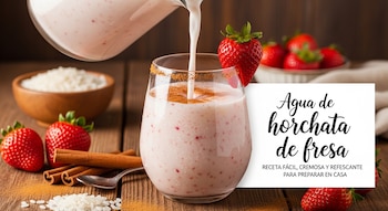 Vaso de agua de horchata de fresa con canela y una fresa en el borde, siendo llenado. Alrededor hay fresas, canela en rama y arroz en una mesa de madera.