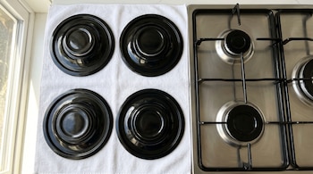 Cuatro tapas de quemadores de estufa de metal negro sobre una toalla blanca. A la derecha, una estufa de acero inoxidable con parrillas y quemadores.