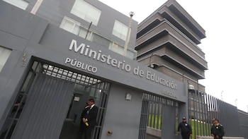 Fachada y portal de ingreso del edificio del Ministerio de Educación, con letreros plateados en la pared y personal de seguridad en la entrada