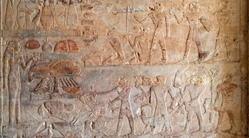 Relieve egipcio en una pared de piedra clara con múltiples figuras talladas, algunas con pigmentos azules, rojos y verdes, y varios símbolos.