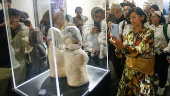 Personas con teléfonos móviles y cámaras observan y fotografían dos figuras de arcilla dentro de una vitrina iluminada
