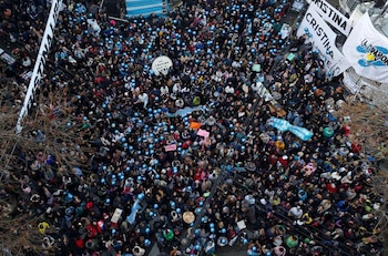 Vista aérea de una densa multitud de personas en una calle; muchas sostienen globos azules. Se aprecian pancartas blancas y ramas de árboles sin hojas