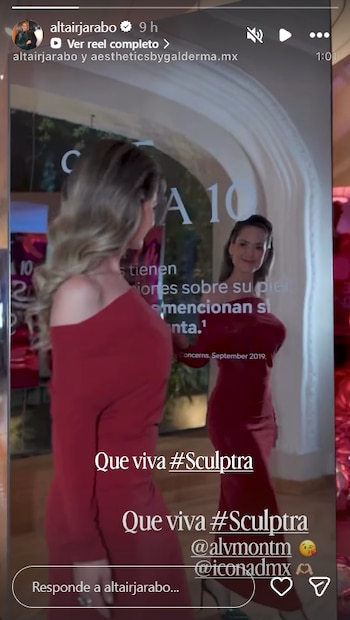 Una mujer con un vestido rojo de manga larga camina frente a una superficie transparente que refleja su figura