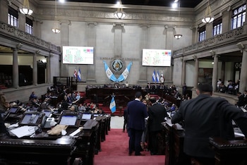Interior de un parlamento con pupitres, personas, dos pantallas mostrando votación, banderas de Guatemala, Costa Rica, Honduras y Panamá, columnas y balcones