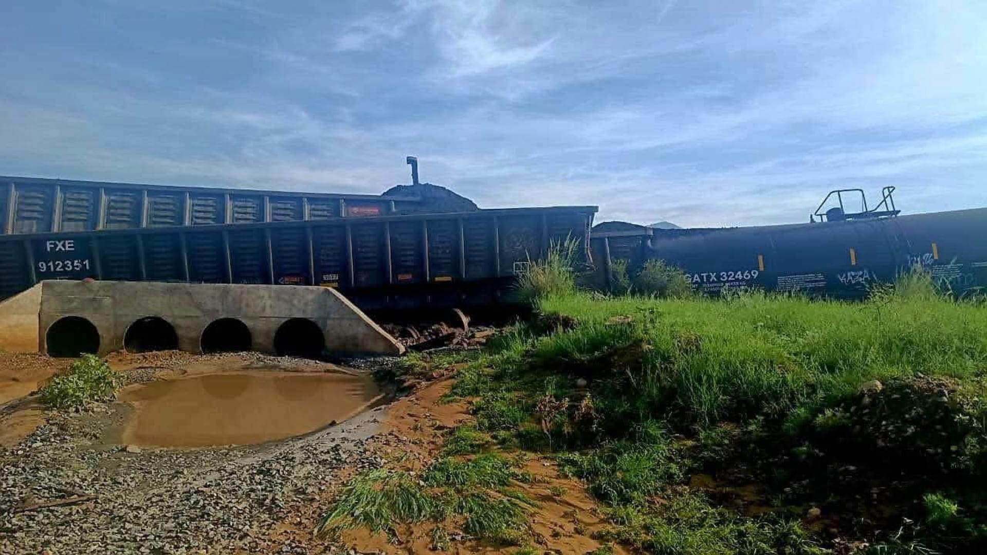 Un tren descarrilado en Sonora muestra varios vagones volcados sobre un arroyo de agua barrosa, algunos con derrame de hidrosulfuro de sodio. (Redes sociales)