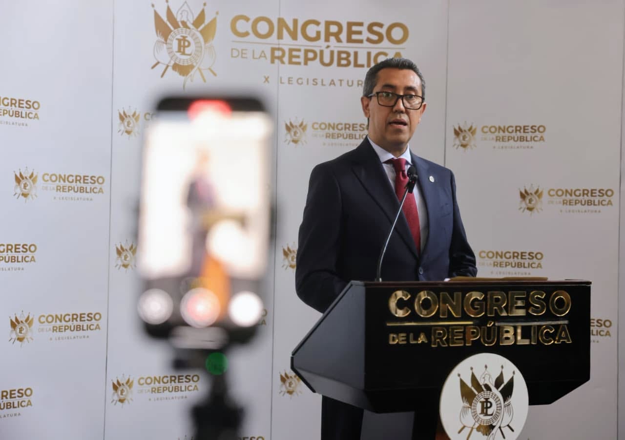 Un funcionario ofrece una declaración en un podio del Congreso de la República mientras un teléfono inteligente graba la intervención desde el primer plano. (Diario de Centroamerica)