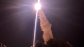 Un misil en ascenso hacia un cielo nocturno con un destello brillante de luz en la punta y una columna de humo en la base