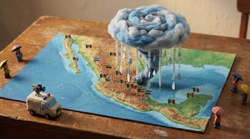 Mapa de México con banderas, una nube de lana con gotas de lluvia, una camioneta de noticias y personas con paraguas sobre una mesa de madera.