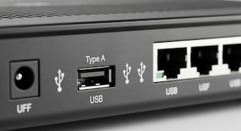 Primer plano de la parte trasera de un router gris oscuro, mostrando un puerto USB Tipo A, varios puertos Ethernet y el conector de corriente.