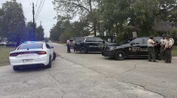 Varios vehículos policiales del condado de Dooly y cuatro agentes en uniforme permanecen sobre una calle asfaltada de zona residencial