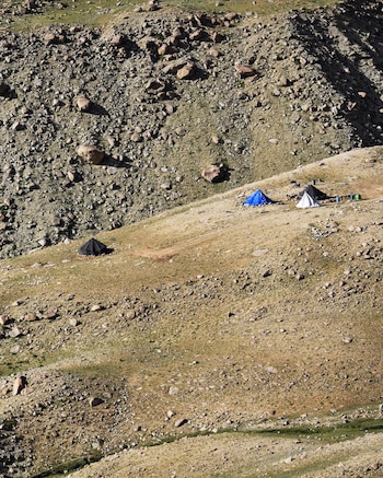 Ladera rocosa con escasa vegetación y cuatro tiendas de campaña de colores azul, blanco y negro
